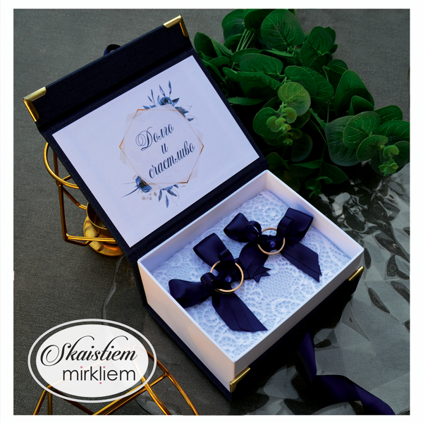 Atvērta tumši zila kāzu gredzenu kastīte ar mežģīņu pamatni un personalizāciju