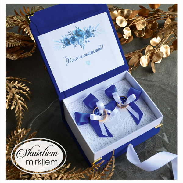 Atvērta zila gredzenu kastīte ar individuālu apdruku un baltu lenti