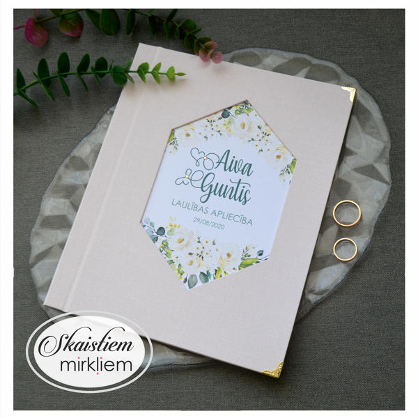 Gaiši rozā laulības apliecības vāki ar ziediem un vārdiem "Aiva un Guntis"