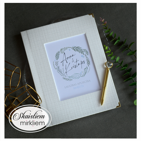 Krēmbalti laulības apliecības vāki ar smalku lapu vainagu un vārdiem "Anna un Kristaps"