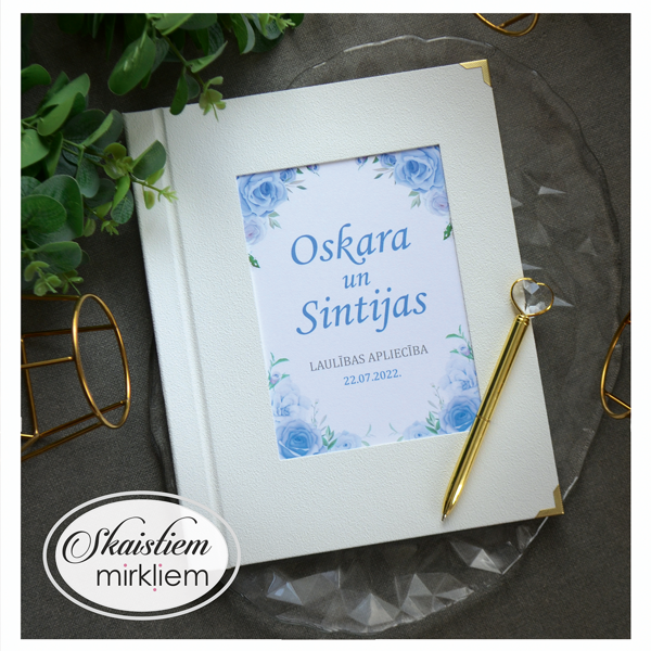 Balti laulības apliecības vāki ar ziliem ziediem un vārdiem "Oskars un Sintija"