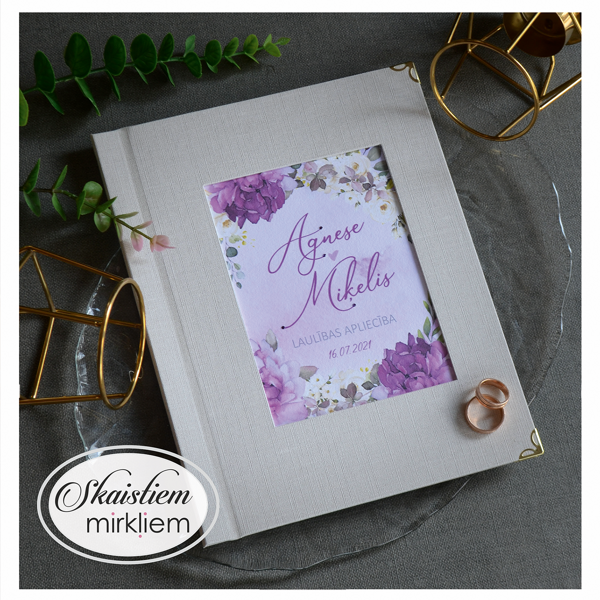 Gaiši pelēki laulības apliecības vāki ar ziedu motīvu un vārdiem "Agnese un Miķelis"