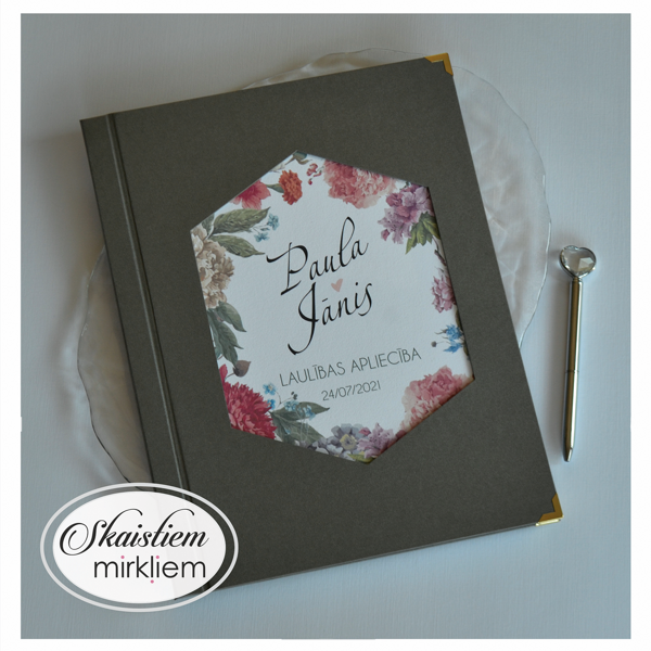 Pelēki laulības apliecības vāki ar sešstūra rāmi, ziediem un vārdiem "Paula un Jānis"