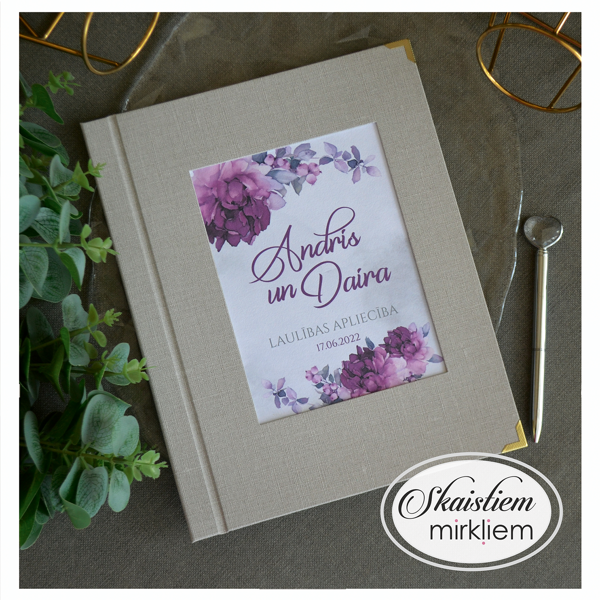 Pelēki laulības apliecības vāki ar violetu ziedu kompozīciju un vārdiem "Andris un Daira"