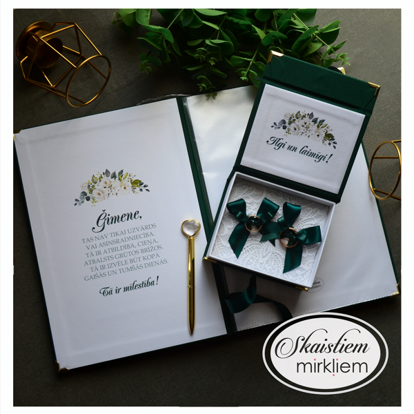 Atvērta laulības apliecības mape un pieskaņota gredzenu kastīte ar tekstu iekšpusē