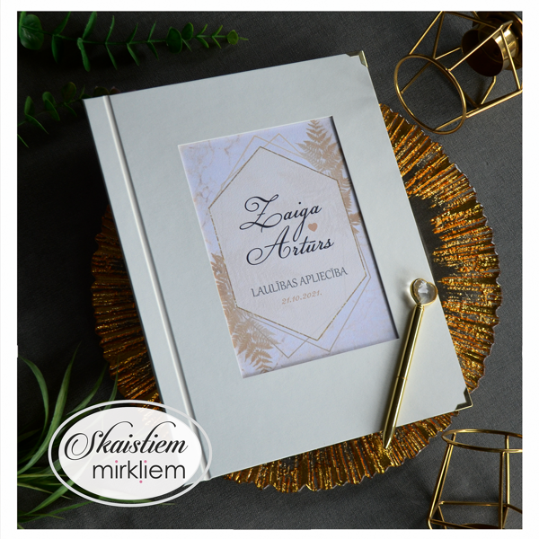 Gaiši krēmkrāsas laulības apliecības vāki ar zelta detaļām un vārdiem "Zaiga un Artūrs"