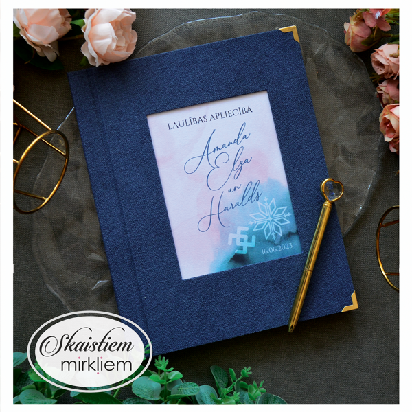 Tumši zili laulības apliecības vāki ar akvareļu pludinājumu, latviskām zīmēm un vārdiem