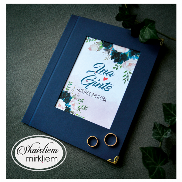Tumši zili laulības apliecības vāki ar ziliem un rozā ziediem un vārdiem "Ina un Gints"