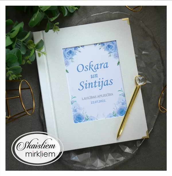 Balti laulības apliecības vāki ar ziliem ziediem un vārdiem "Oskars un Sintija"
